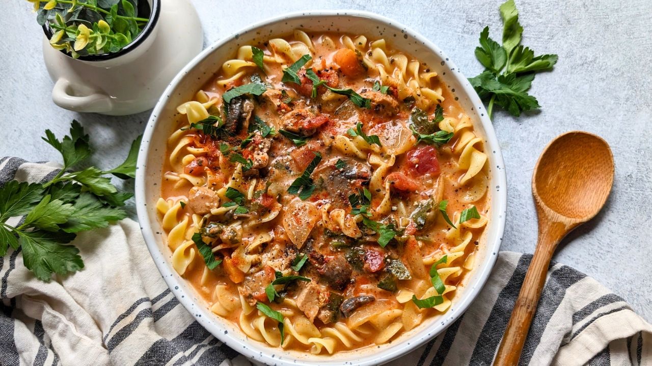 low sodium paprika chicken stew with egg noodles and fresh vegetables in a bowl with a wooden spoon