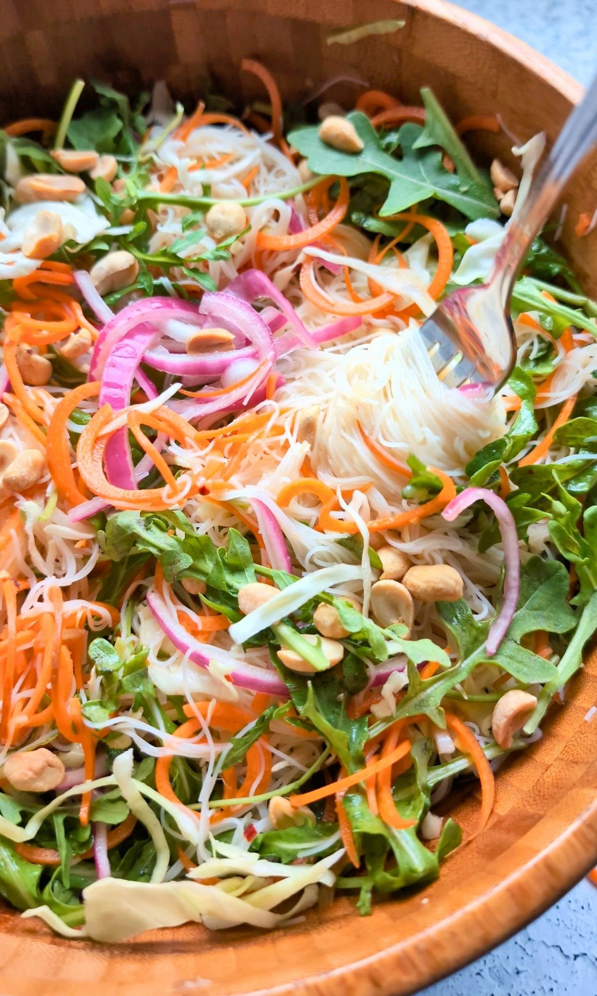a fork twirling a low sodium asian inspired noodle salad with pickled onions carrots and arugula