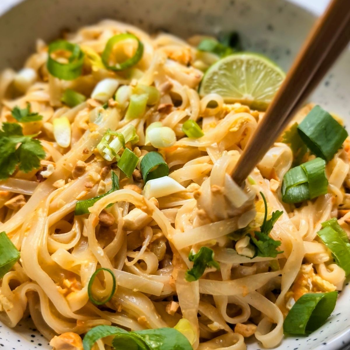 chopsticks twirling a large bundle of noodles dressed in a low sodium peanut sauce with unsalted peanuts and fresh limes