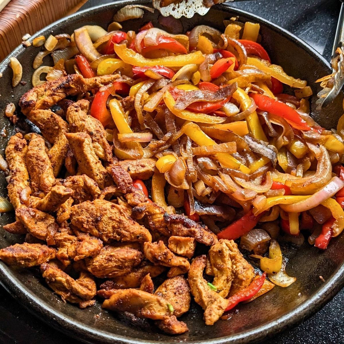 a cast iron skillet of low sodium chicken fajitas with red onions sweet yellow onions and bell peppers charred to perfection
