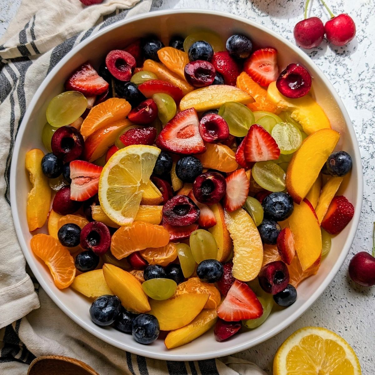 a bowl of fruit salad with berries, cherries, oranges, peaches, and green grapes