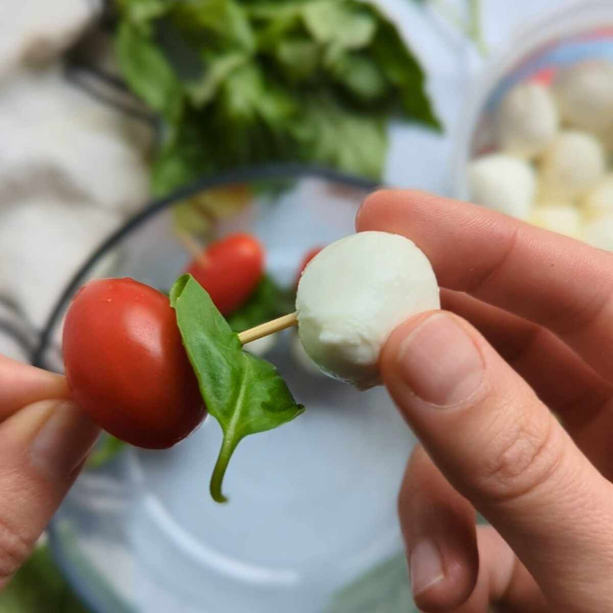 fresh mozzarella balls being placed on a toothpick with basil and a cherry tomato