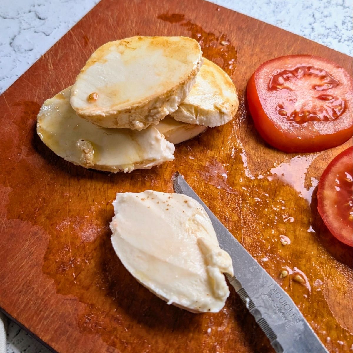 a cutting board with mozzarella cheese being sliced with tomatoes.