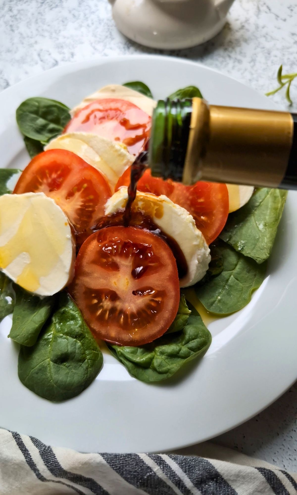 balsamic vineger being poured over fresh tomato slices with mozzarella cheese and basil on a plate.