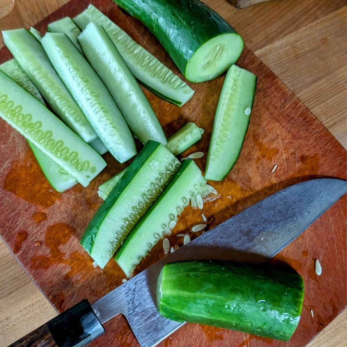 fresh cucumbers sliced into spears with a japanese steel knife on a cutting board.