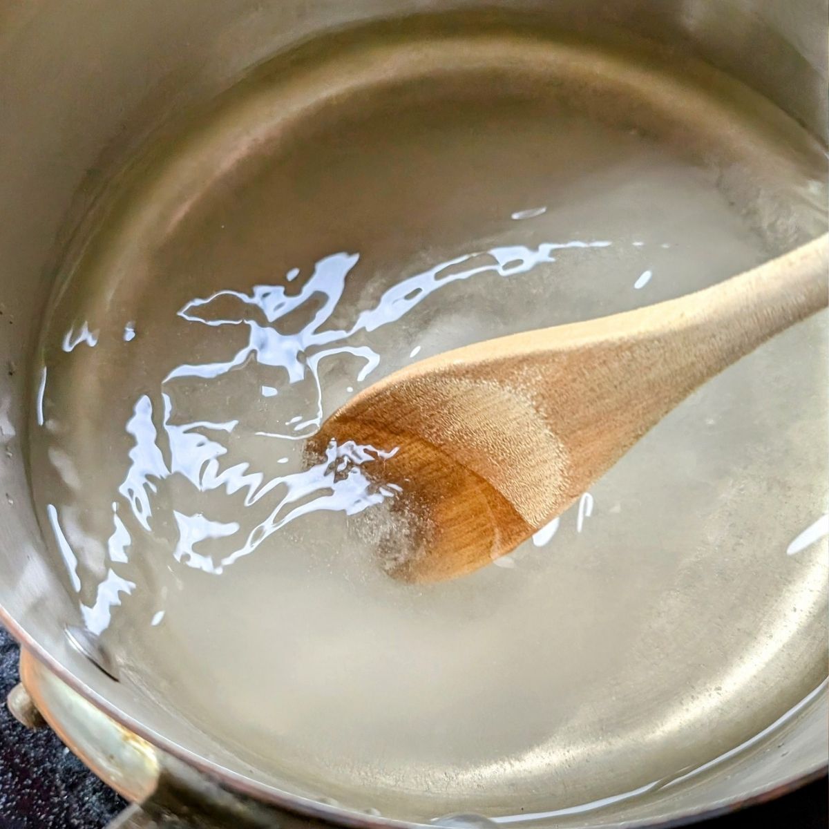 a wooden spoon stirringa pan of sugar and salt and water for pickle brine.