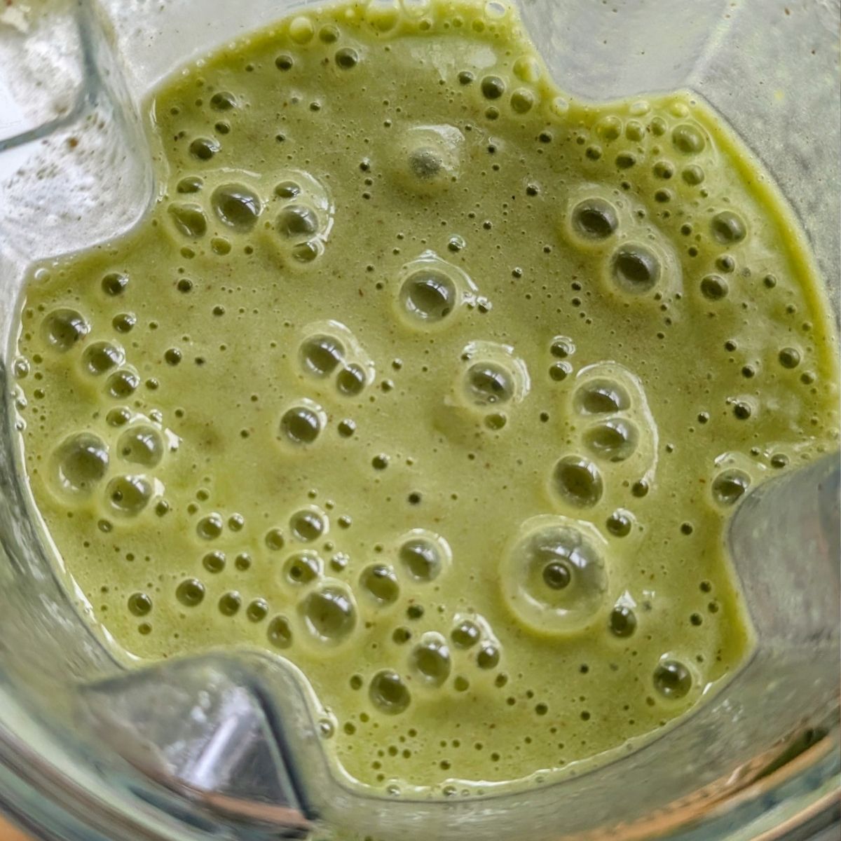 a blender full of a tasty green smoothie blend with baby spinach pineapple and protein powder with mango and ice.