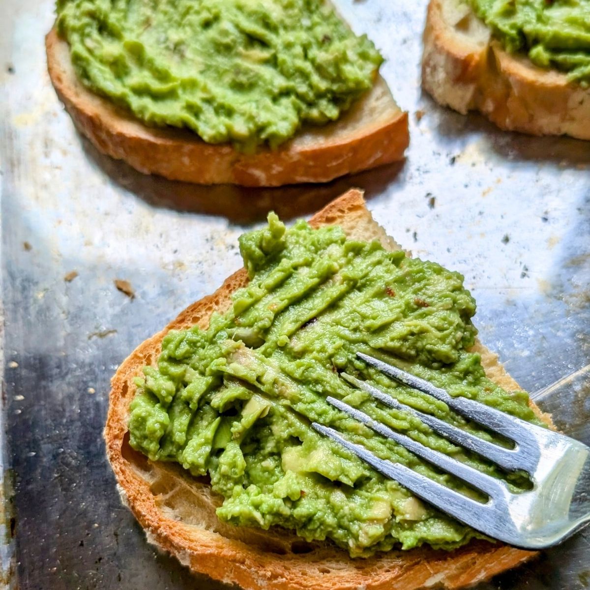 a fork mashing avocado over toasted bread rubbed with garlic.