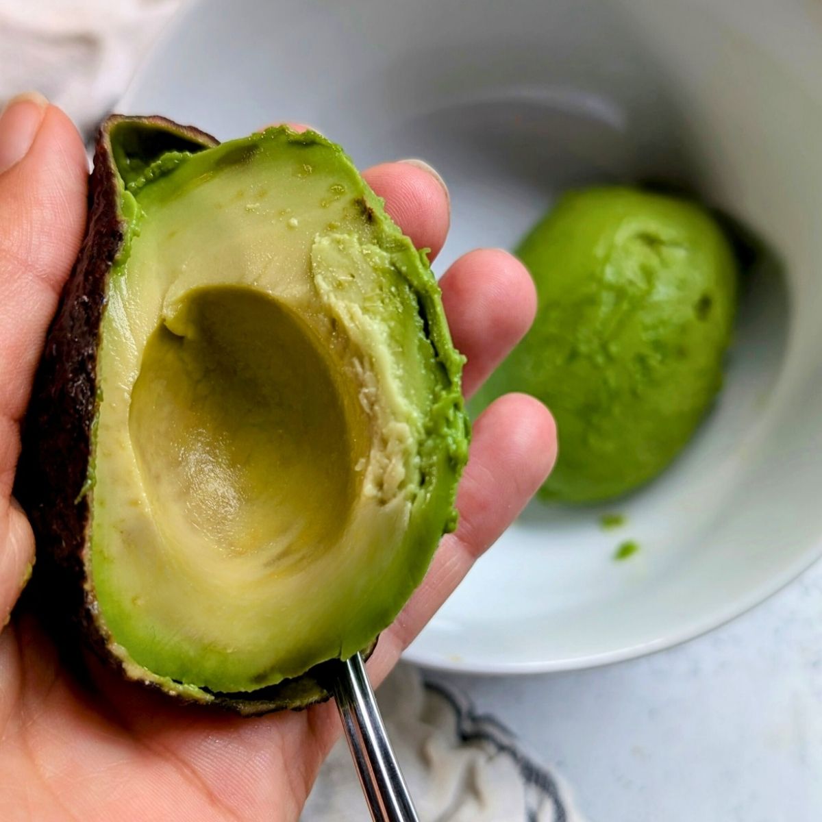 a ripe avocado being scooped out and into a bowl.