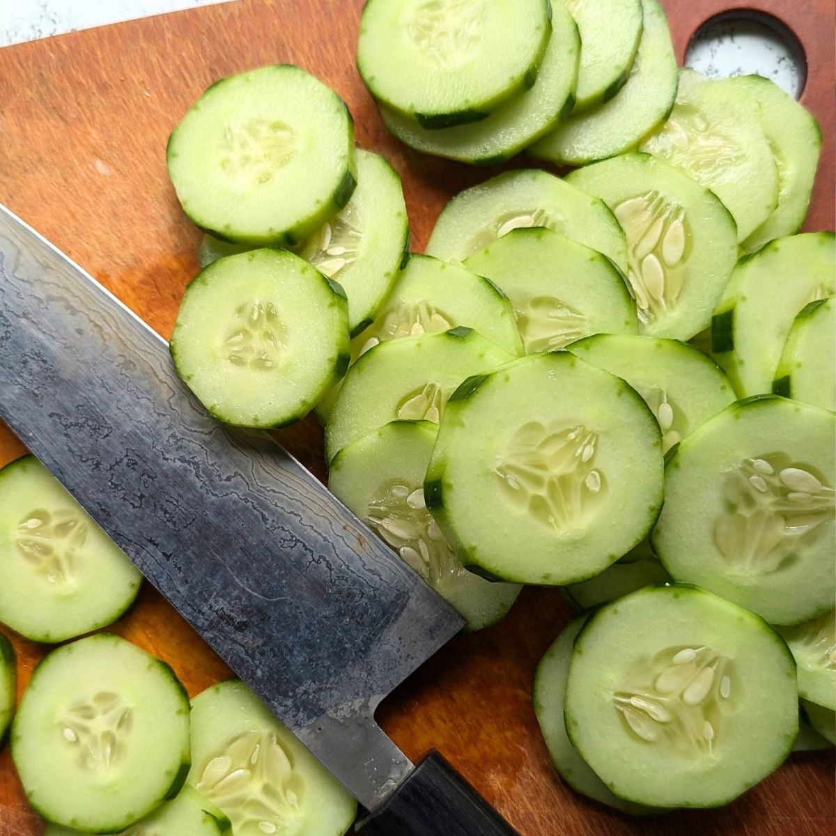 a knife thinly slicing cucumbers for this salad.