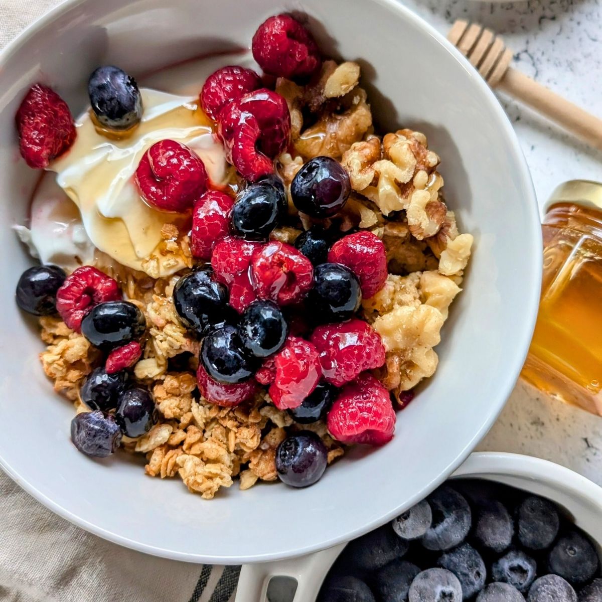 low sodium granola yogurt bowl recipe with blueberries and raspberries and honey.