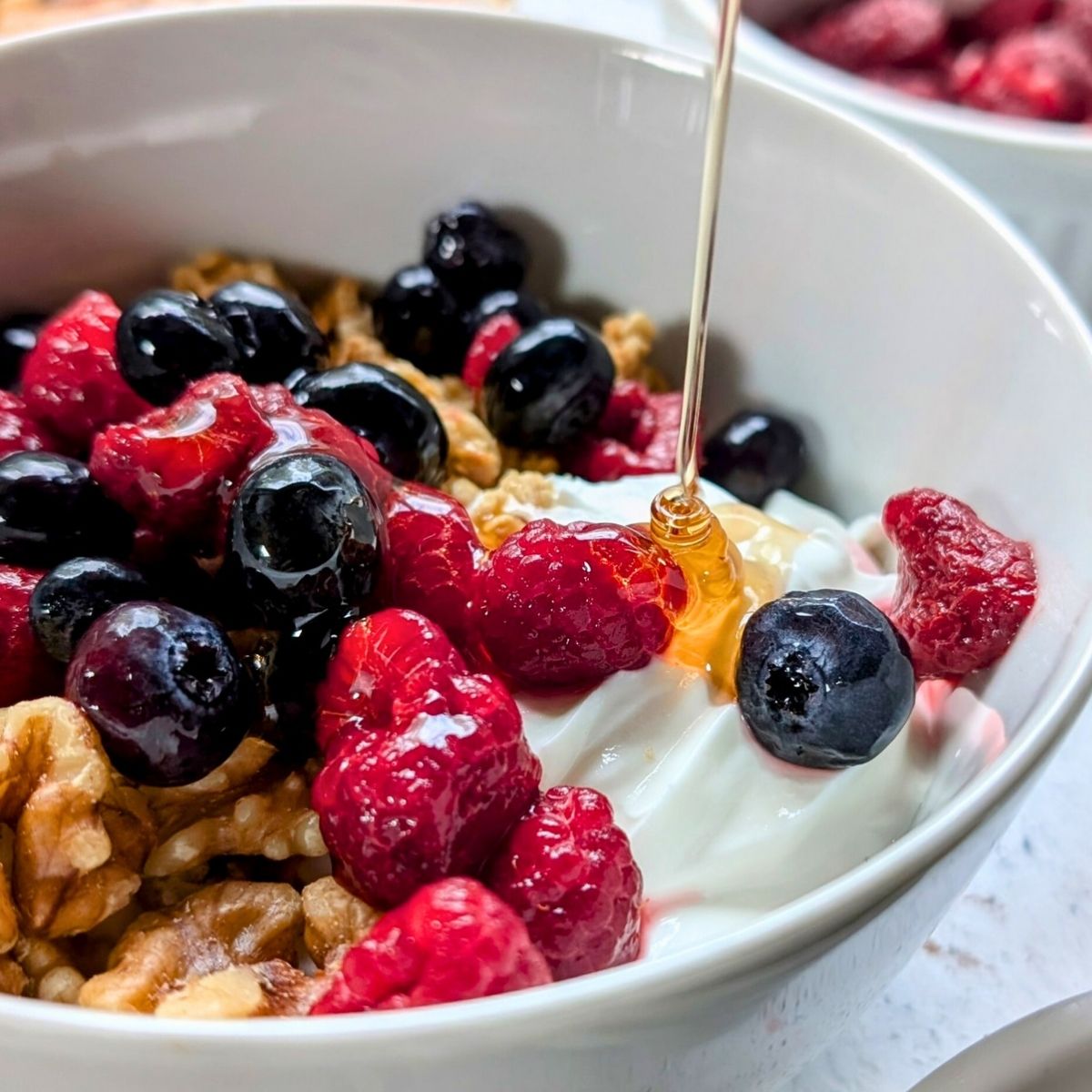 fresh honey being drizzled over a no salt breakfast bowl with yogurt blueberries and raspberries.