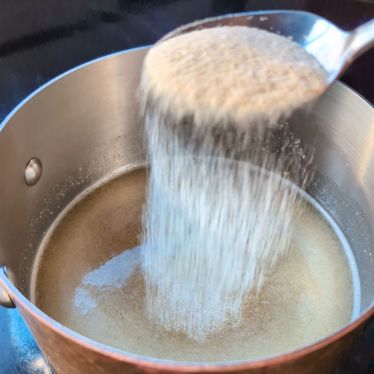 onion powder, garlic powder, and black pepper being added to a pot of stock and roux to make unsalted gravy.