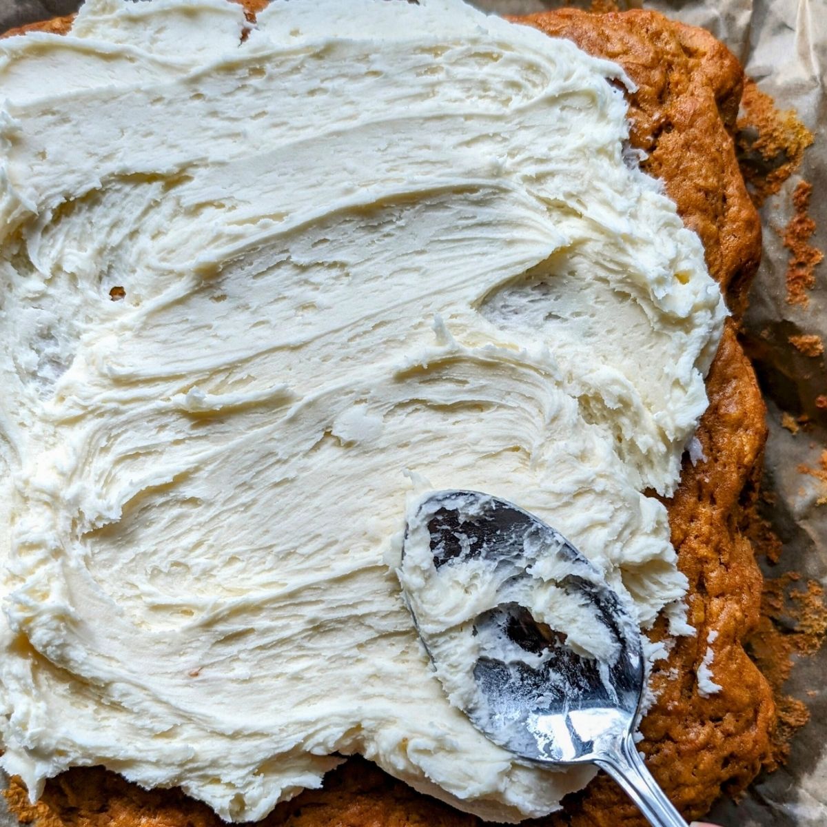 a carrot cake being frosted with thick low sodium buttercream icing with a spoon.