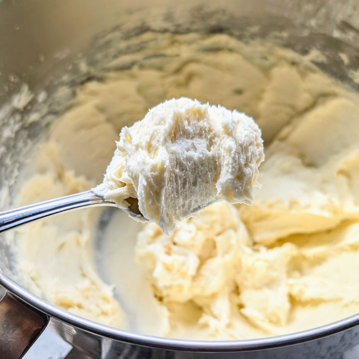 a spoon scooping low sodium buttercream frosting for desserts like chirstmas cookies or carrot cake.