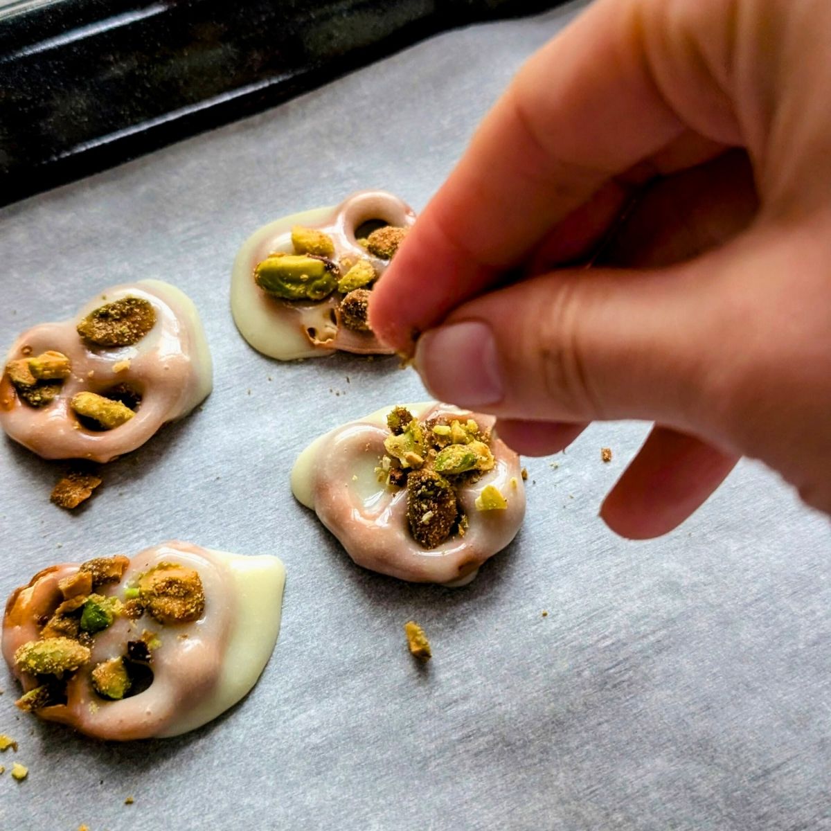 a hand sprinkling crushed cinnamon sugar nuts on top of the white chocolate pretzels for low sodium dessert.