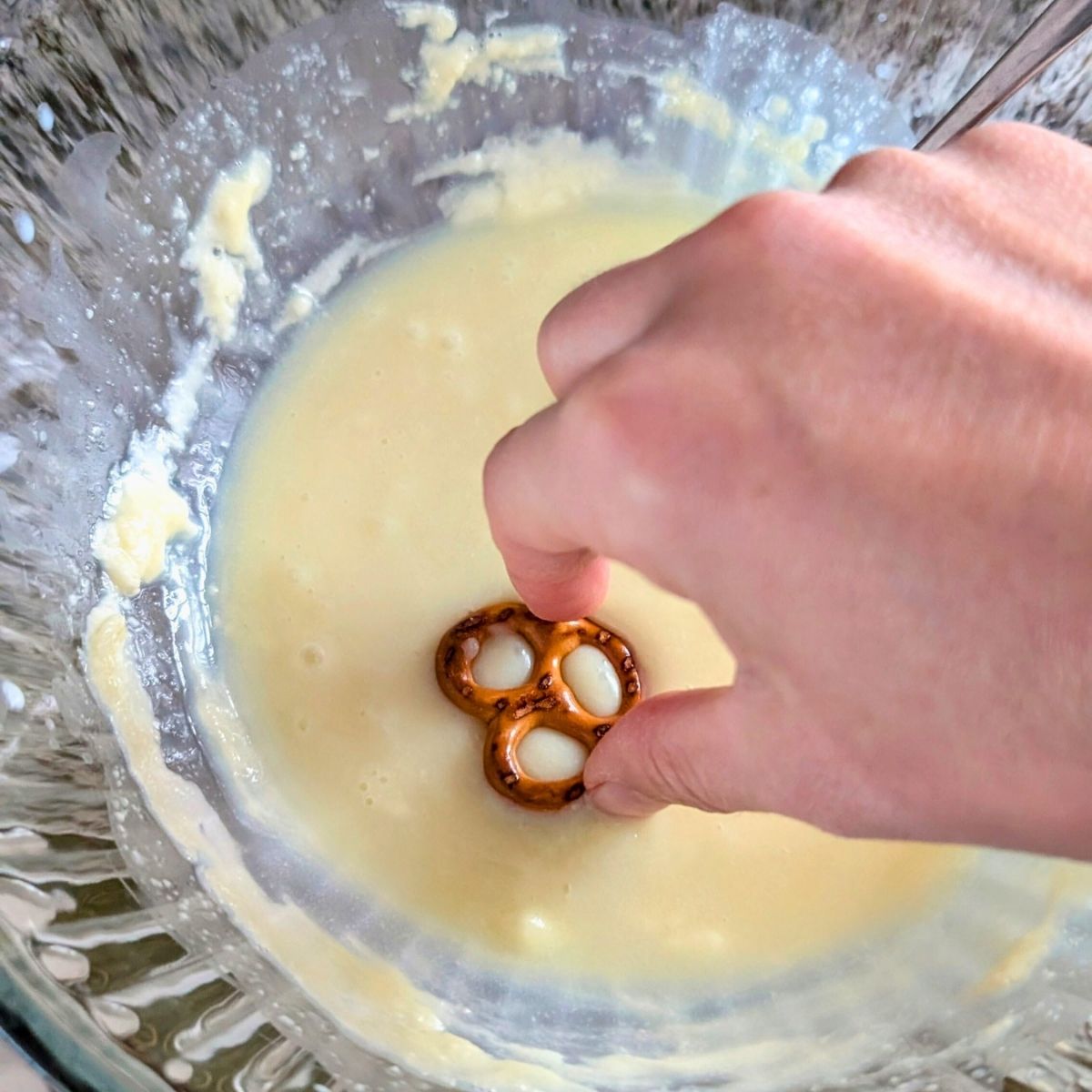 a hand dipping an unsalted pretzel in white chocolate melted in a bowl.