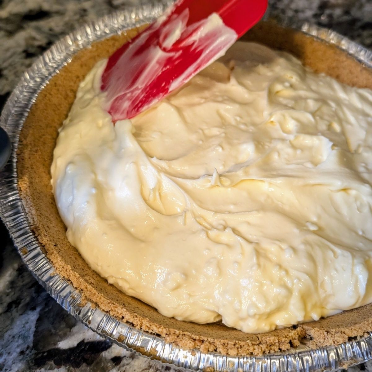 a spatula spreading low sodium cheesecake filling into a pie crust in an even layer.