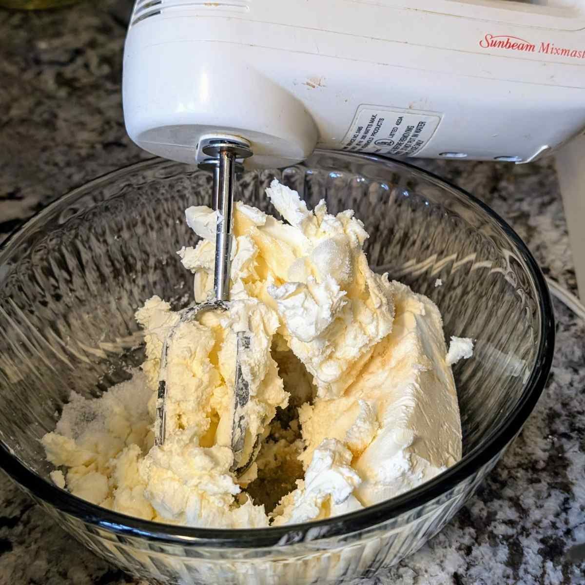 softened cream cheese mixed in a bowl being whipped by a hand mixer for low sodium cheesecake.