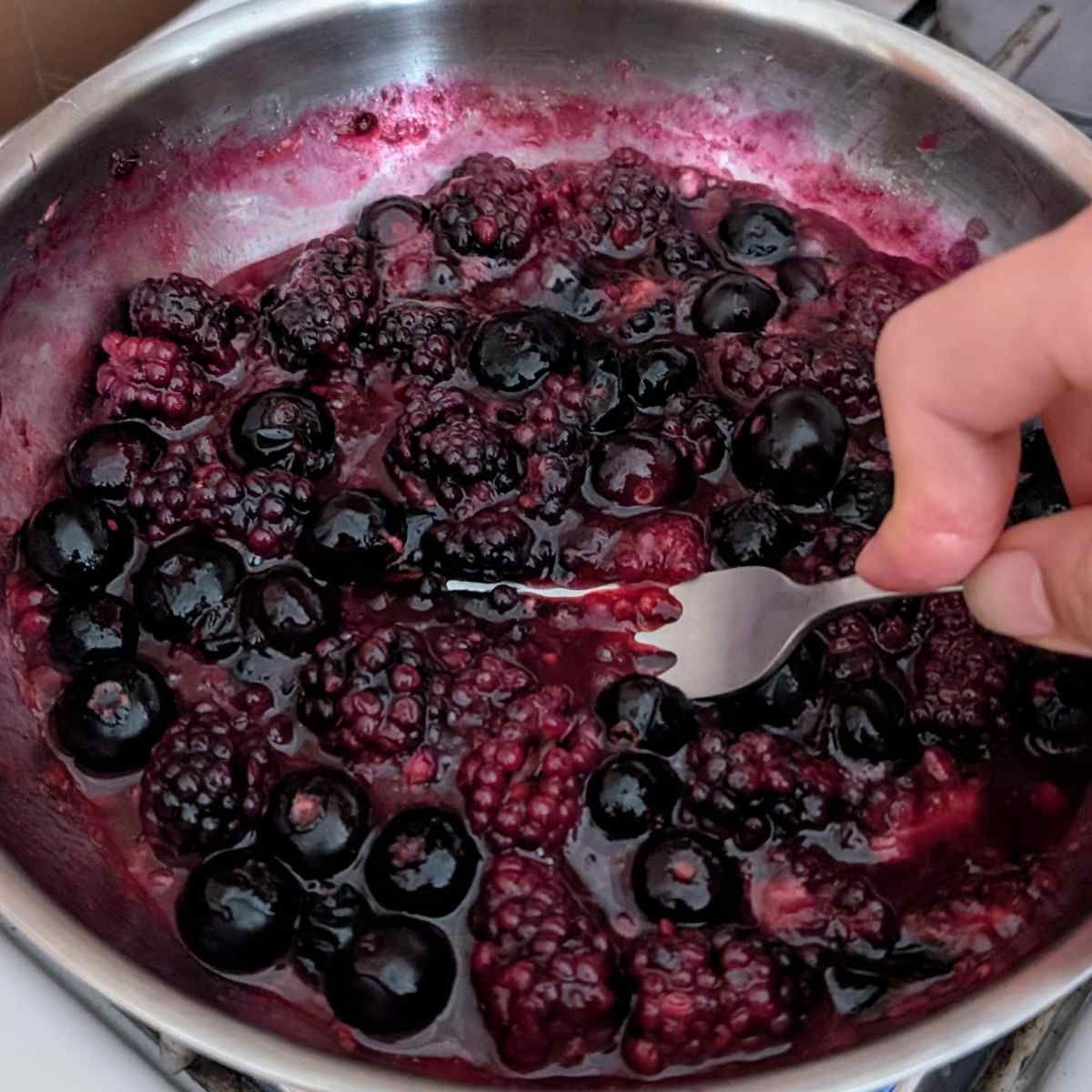 berries in a pan to make berry compote mashed with a fork to release their juices.