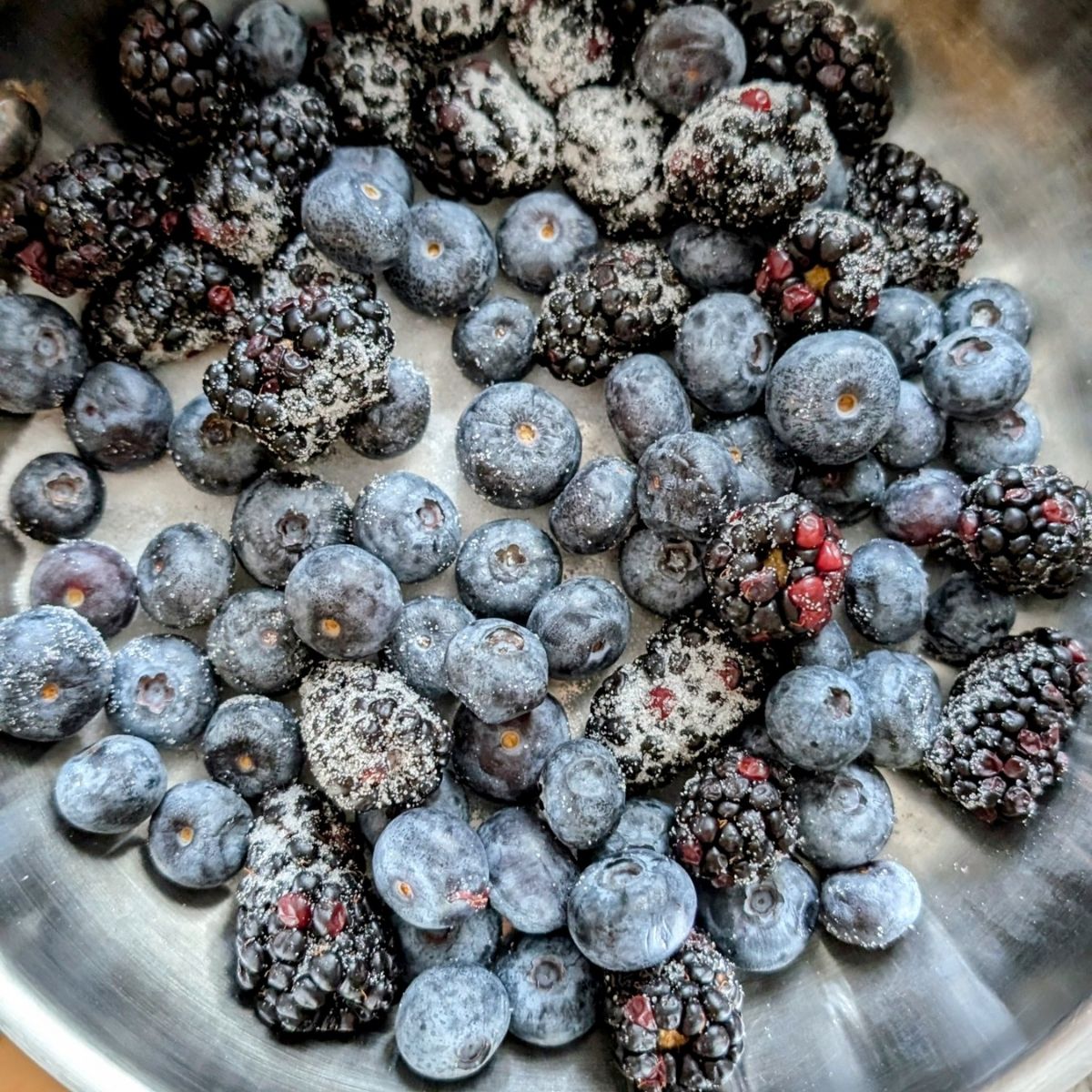 blueberries and blackberries with sugar in a bowl to make cheesecake topping for low sodium berry cheesecake.