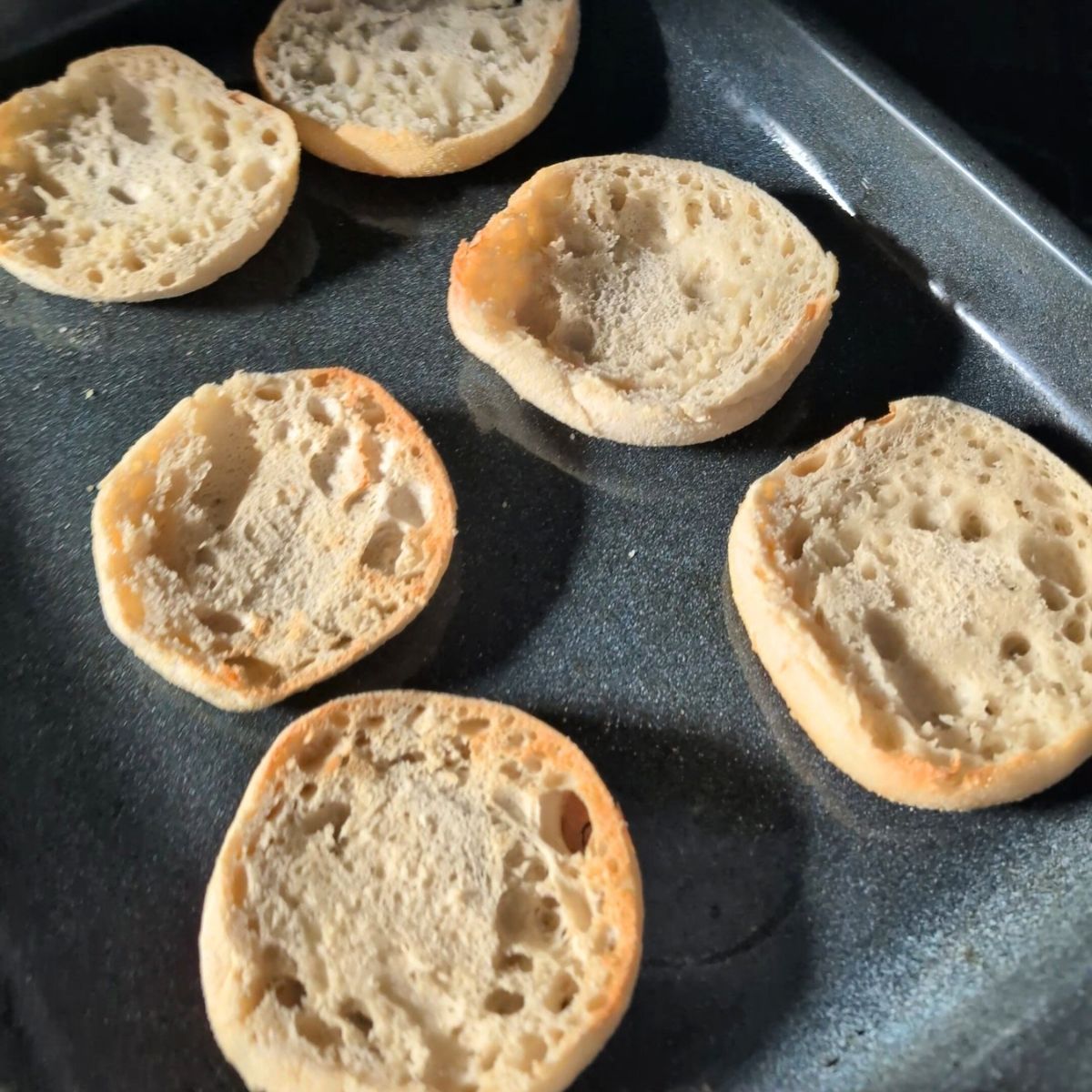 toasted english muffins on a sheet pan being broiled in the oven