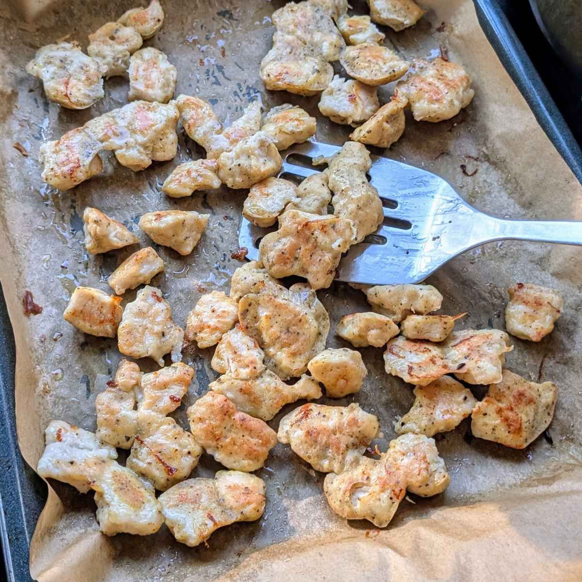 oven baked crispy chicken pieces being tossed with a spatula