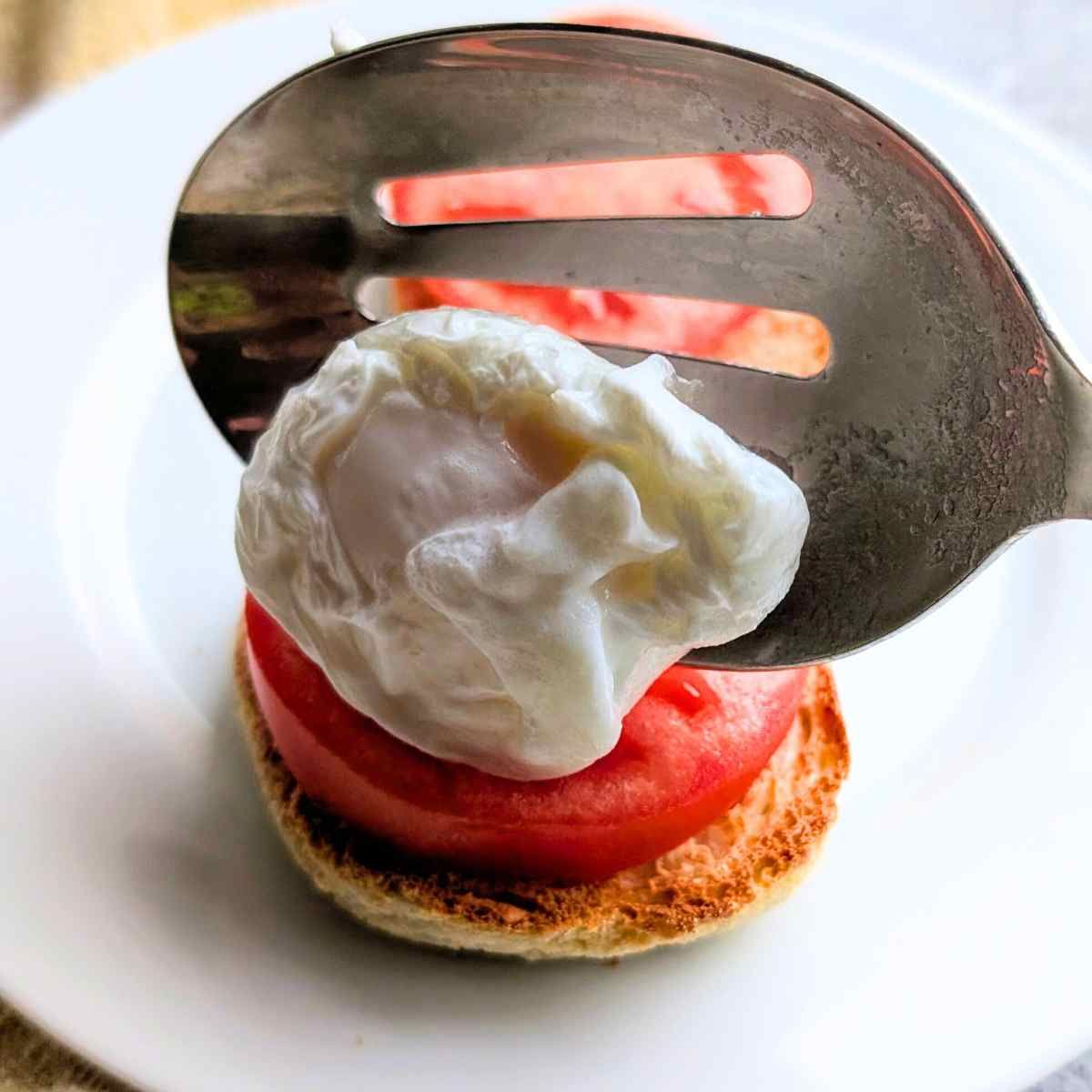 a spoon placing a perfectly poached egg on a low sodium english muffin with tomatoes