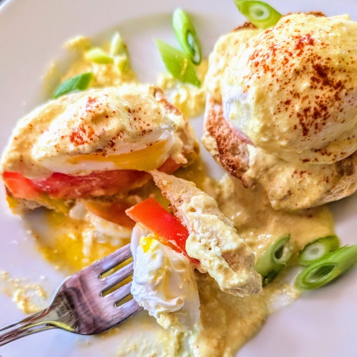 a fork slicing into low salt eggs Benedict smothered in low sodium Hollandaise sauce and fresh tomato and paprika.