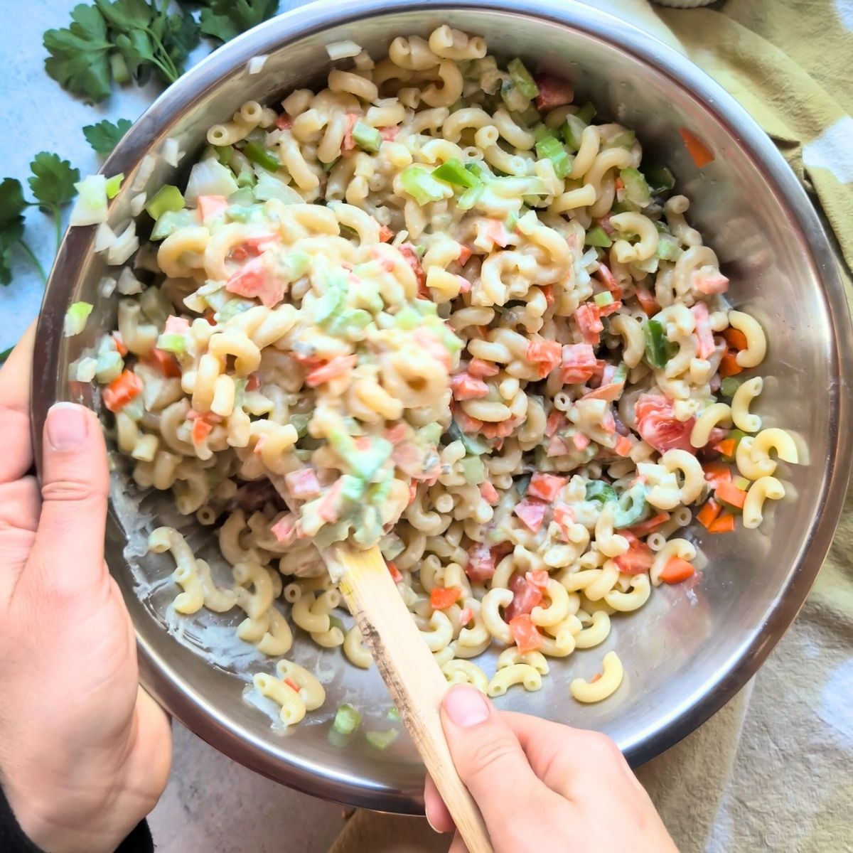 a hand mixing a bowl of salt free macaroni salad with vegetables