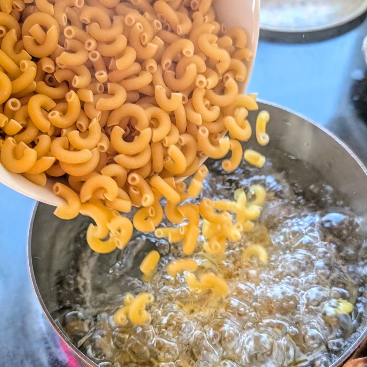 cooked macaroni noodles poured into a bot of boiling water for macaroni salad.