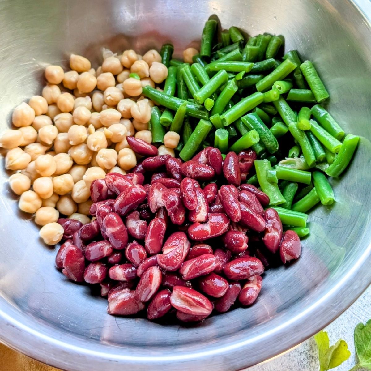 a large bowl of dark red kidney beans, chickpeas, and green beans in a mixing bowl for bean salad.