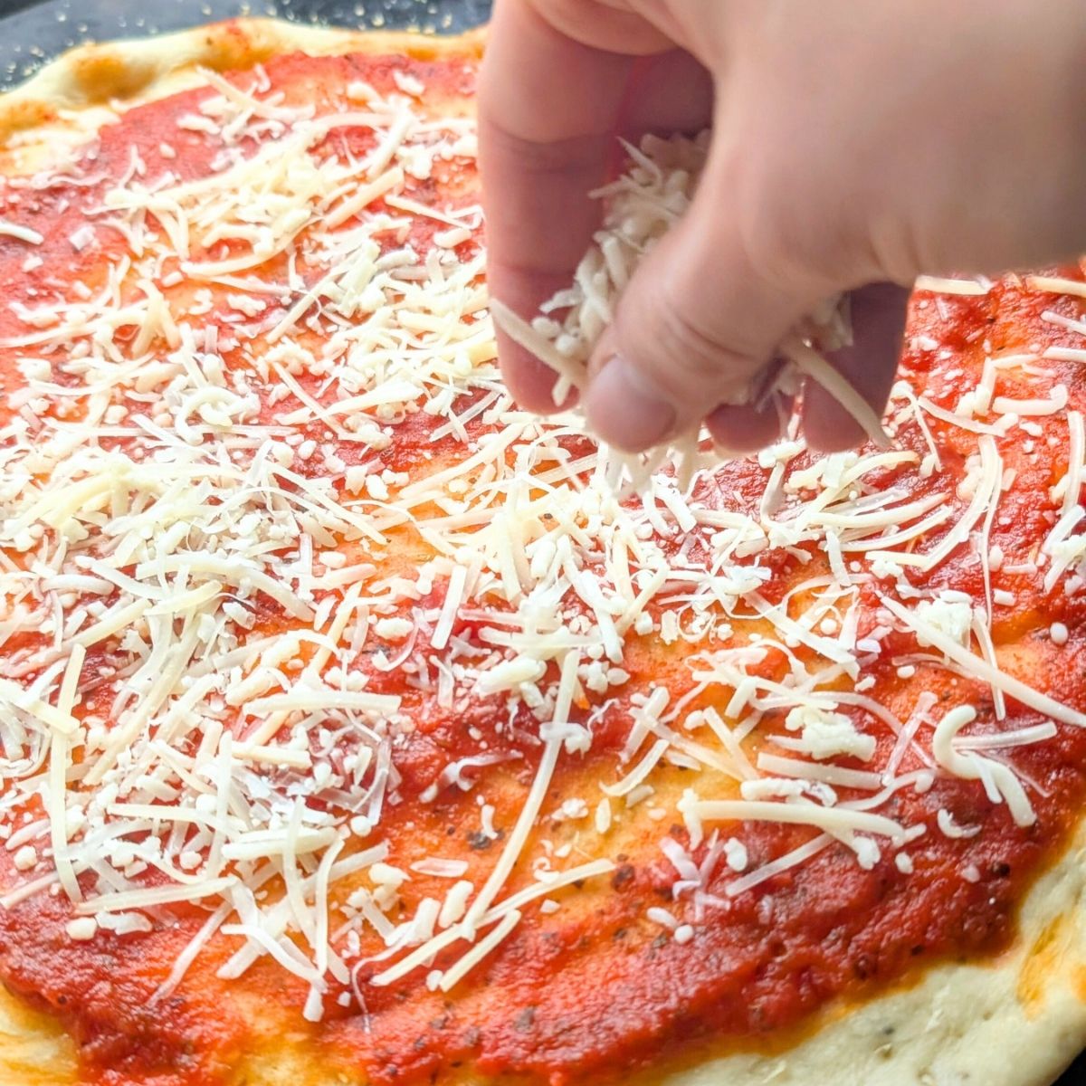 a hand sprinkling low sodium parmesan cheese on pizza dough