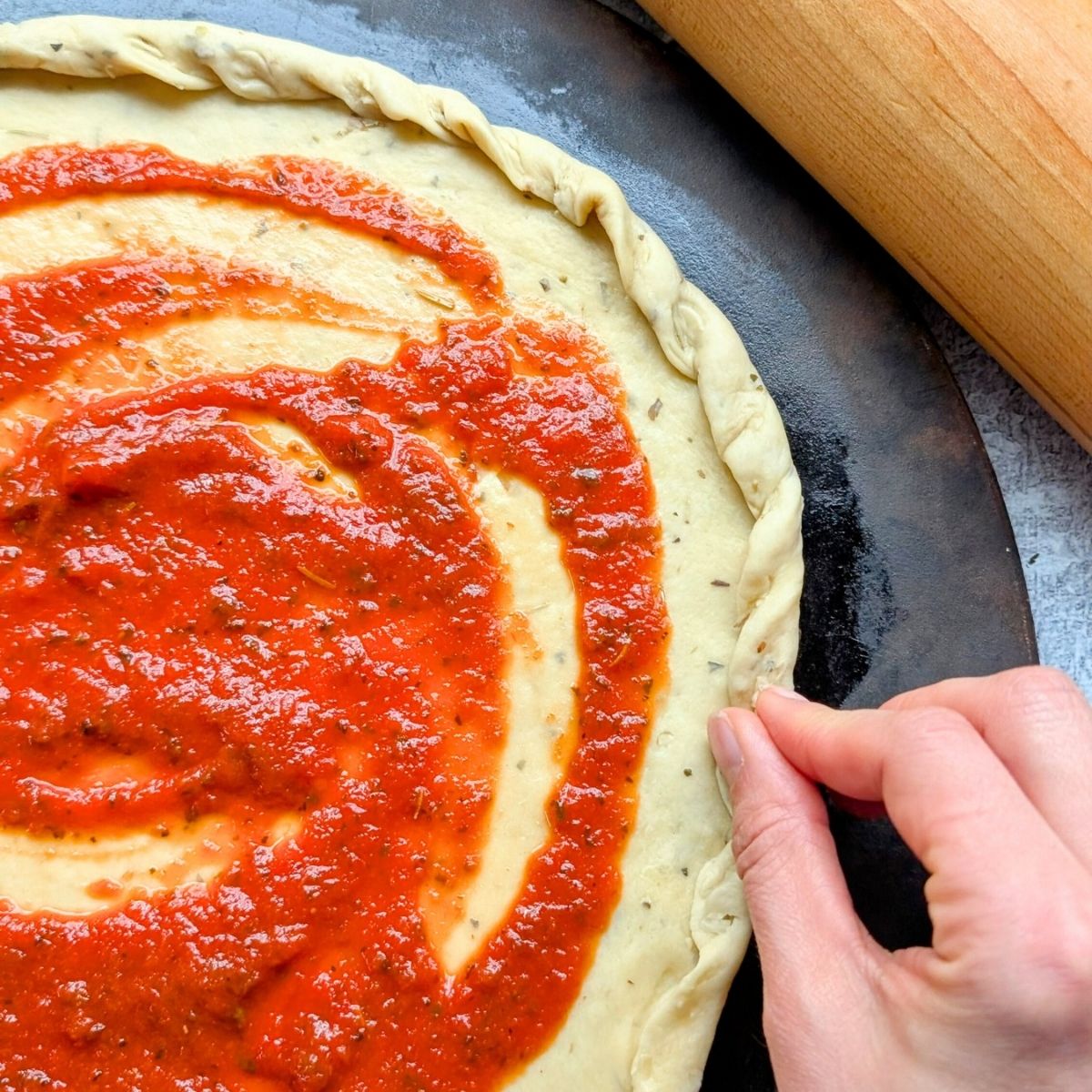 a hand pinching low sodium pizza crust with salt free pizza sauce on top