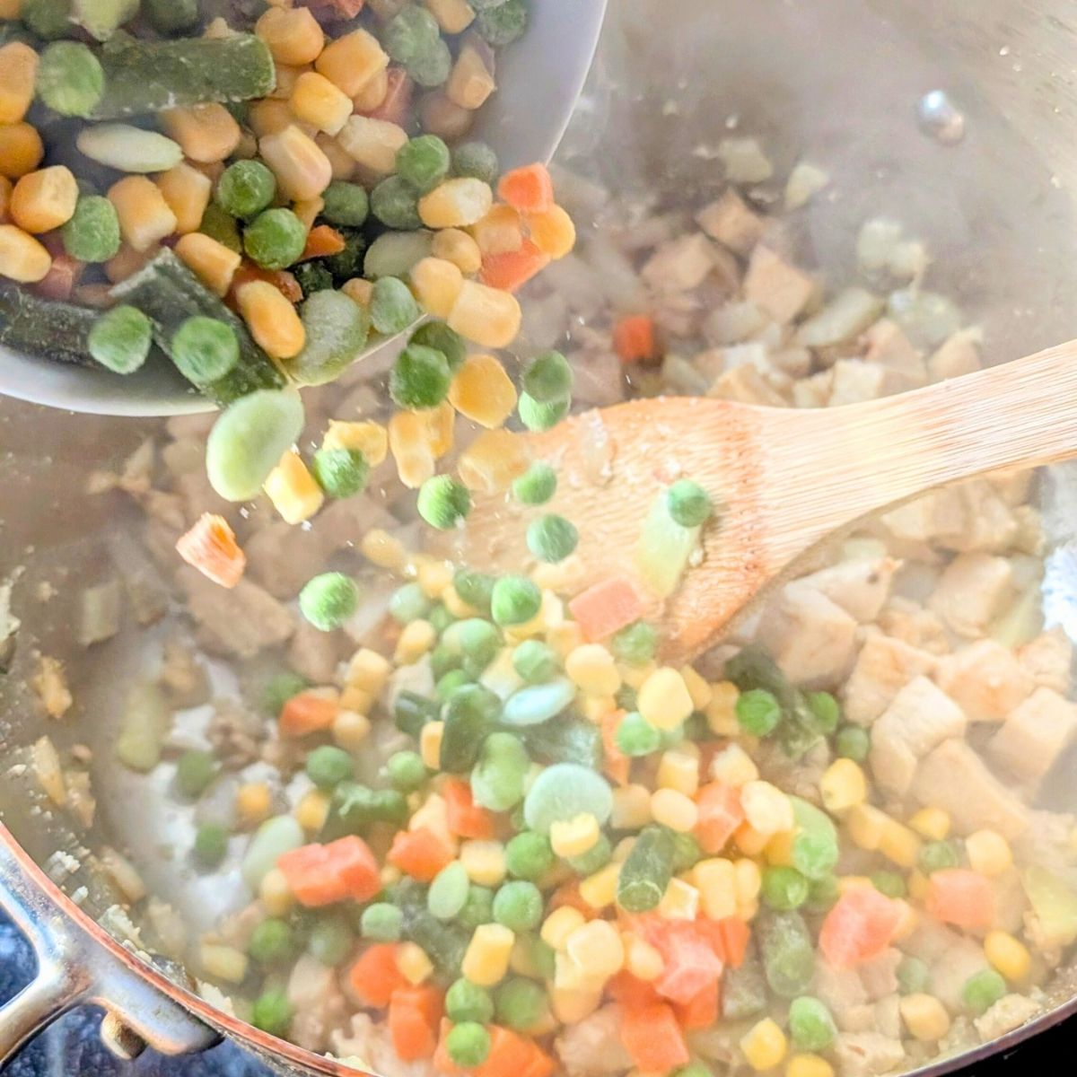 frozen vegetables being added to a pot with cooked chicken for no salt added chicken pot pie