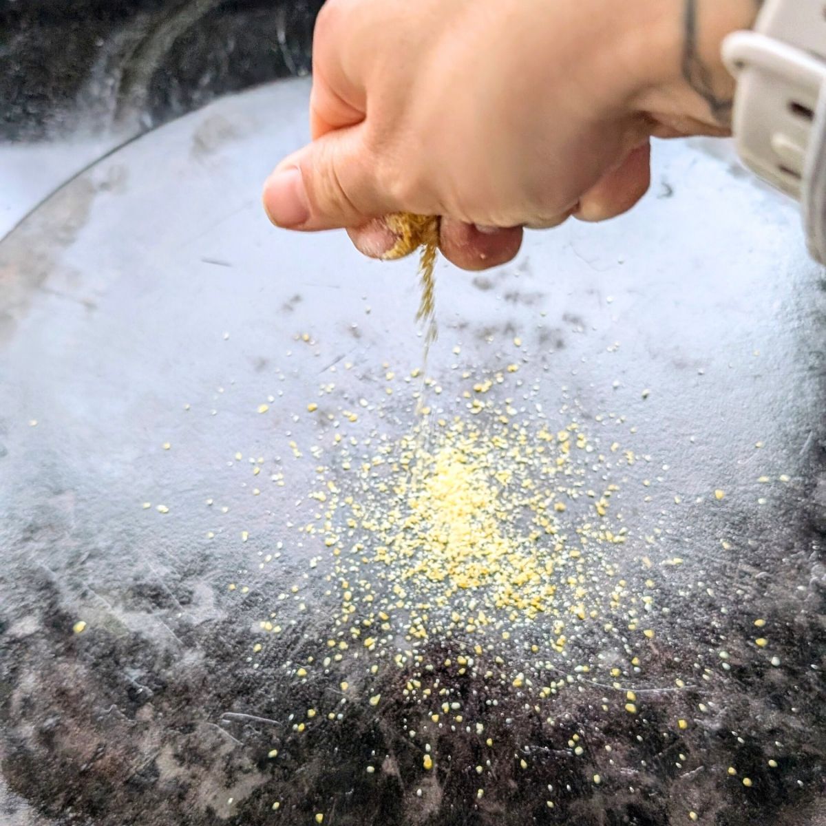 a hand sprinkling low sodium cornmeal on a pizza stone