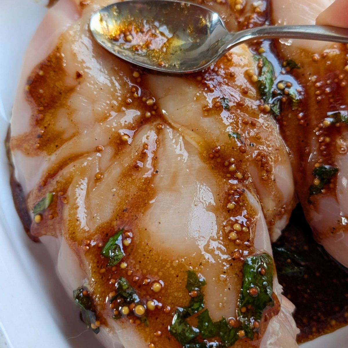 a spoon spreading no salt added balsamic glaze on chicken breasts for a dash diet friendly dinner