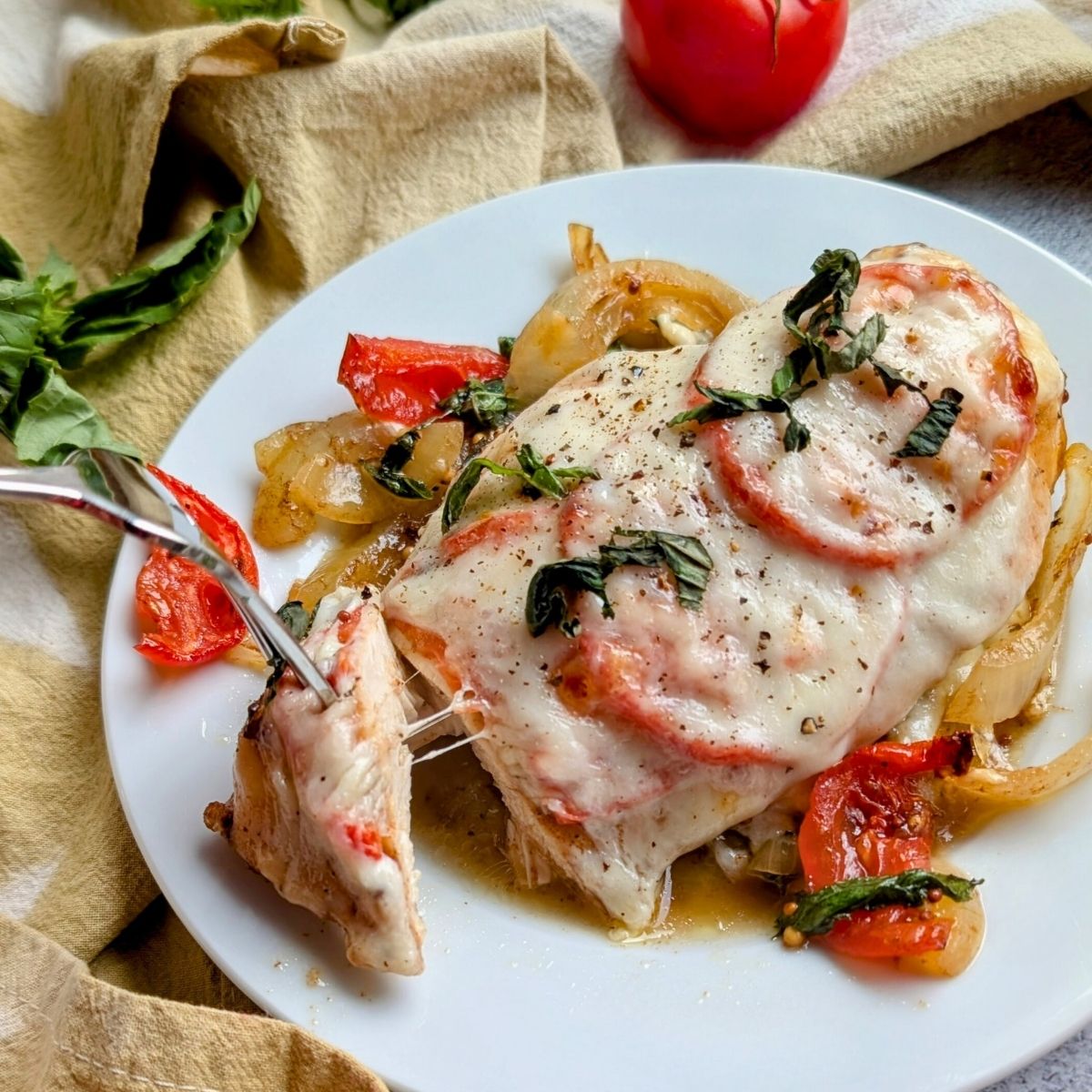 a fork pulling cheese on low sodium italian chicken caprese with fresh basil and sliced tomatoes