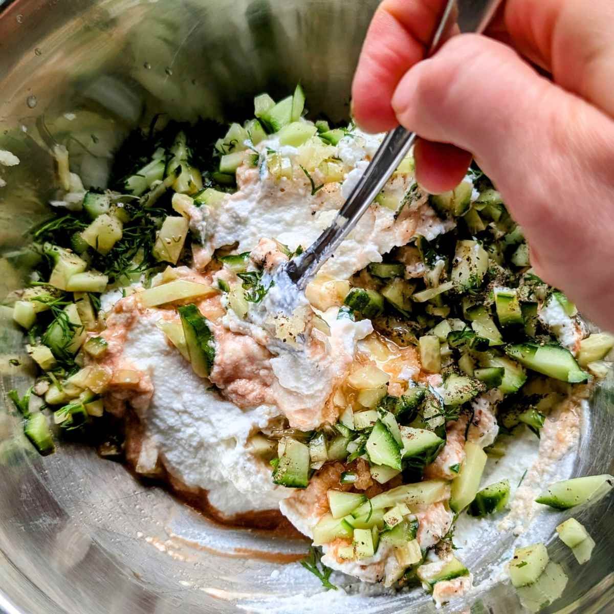 a hand stirring a bowl of salt free cucumber yogurt sauce low sodium condiment and dip for meat.