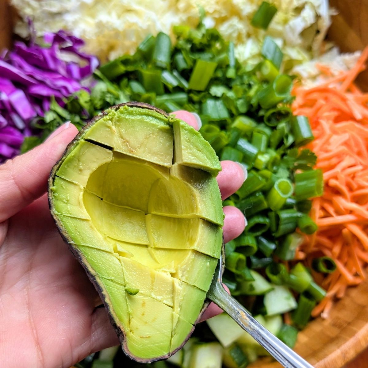 a hand slicing avocado and scooping it into a bowl for a delicious low sodium salad addition