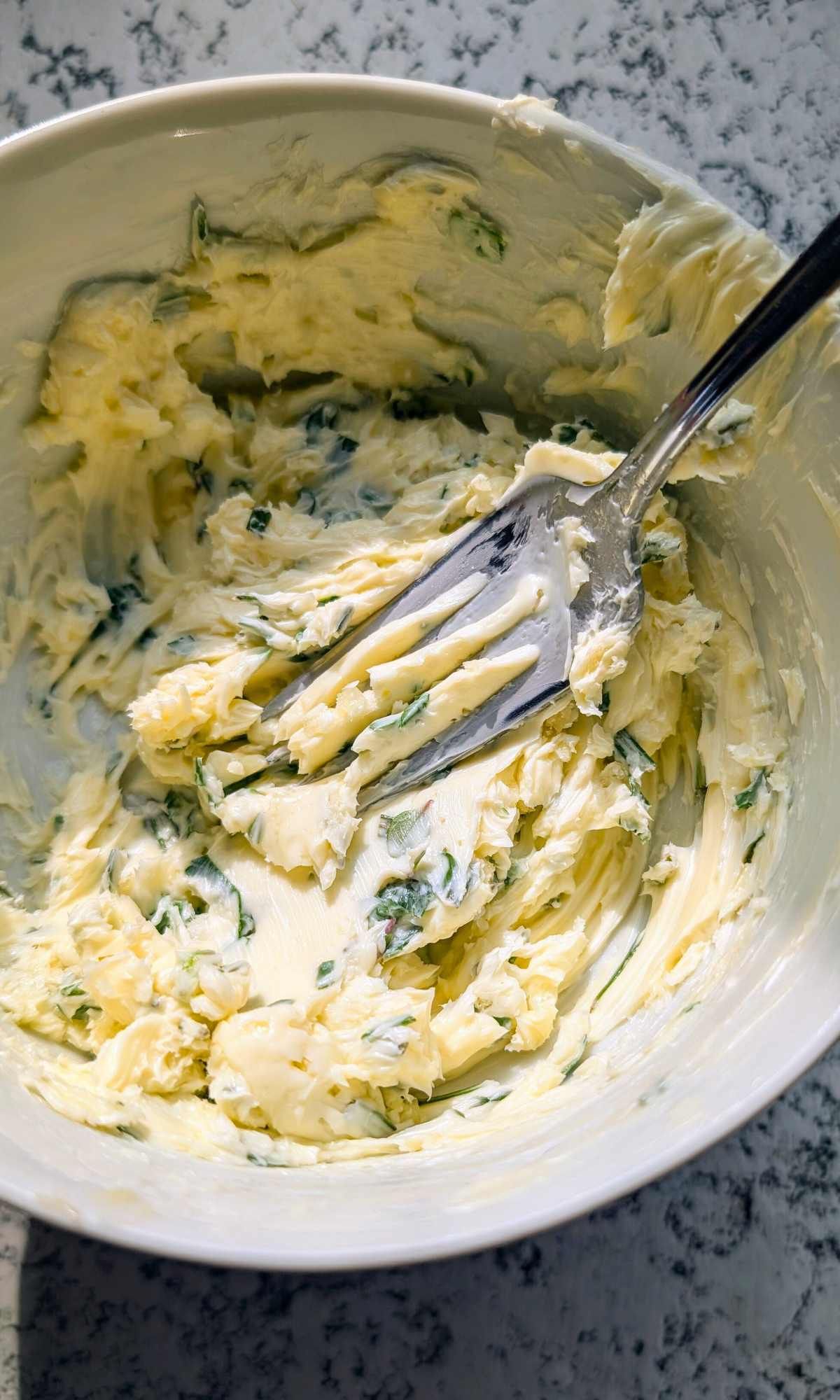 a mixing bowl of unsalted butter with fresh parsley, rosemary, and thyme with fresh garlic for salmon.