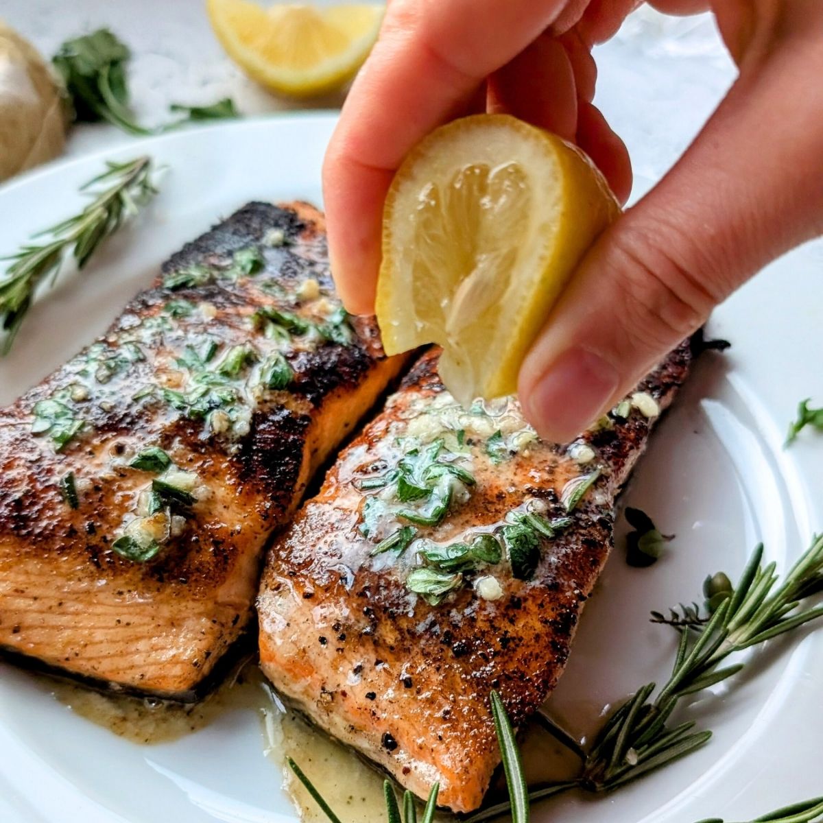 garlic butter salmon with fresh lemon squeezed on top with fresh herbs.