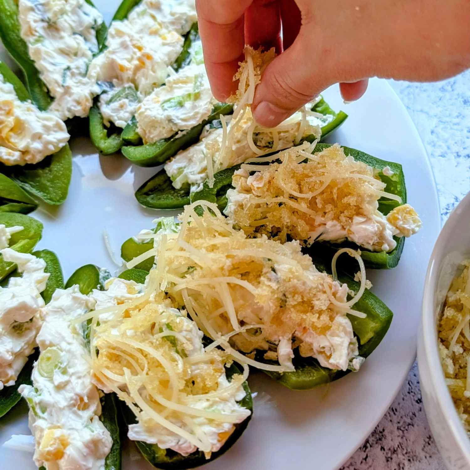 a hand topping low sodium jalapeno peppers filled with cream cheese and stuffed and topped with cheese.