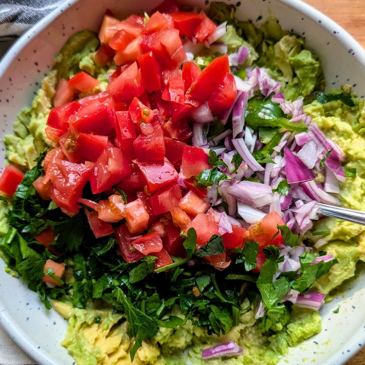 a bowl of unmixed guacamole with tomatoes, cilantro, red onion, and no added salt.
