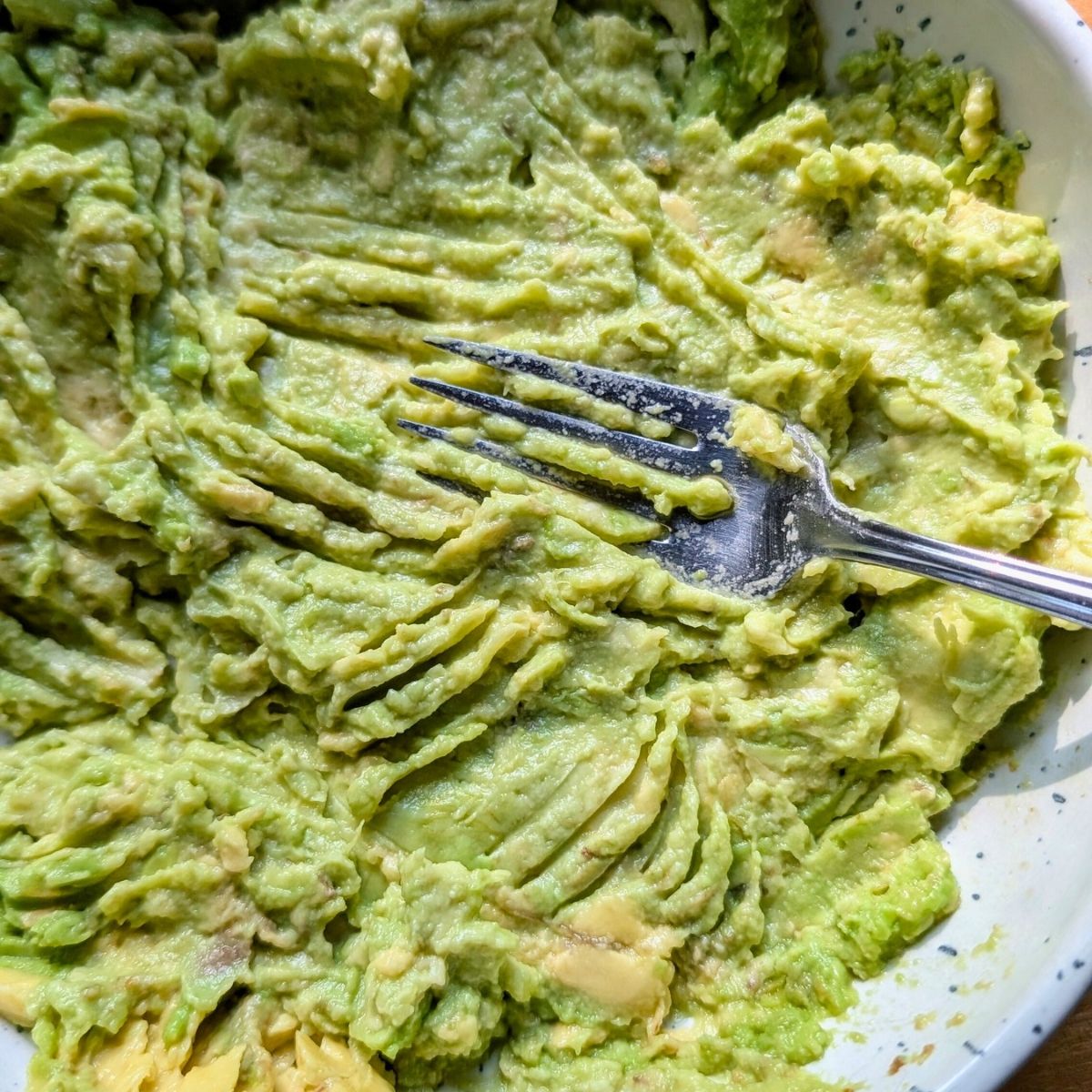 mashed avocado with a fork in a bowl to make low sodium appetizer dip