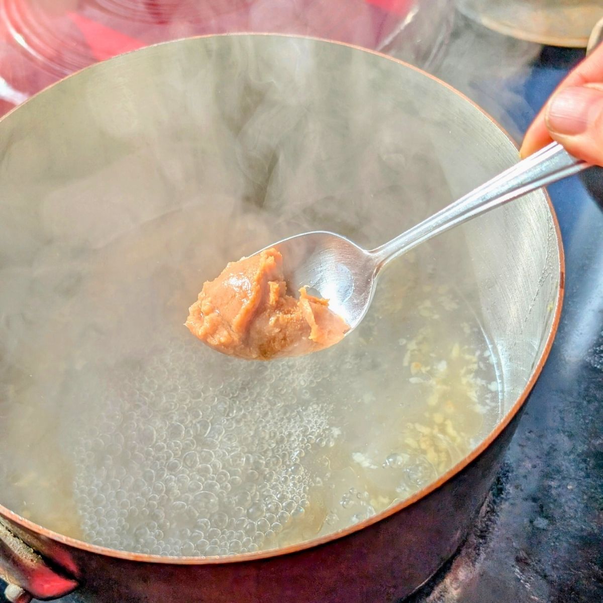 miso paste being added to a pot of broth and garlic and sesame oil.