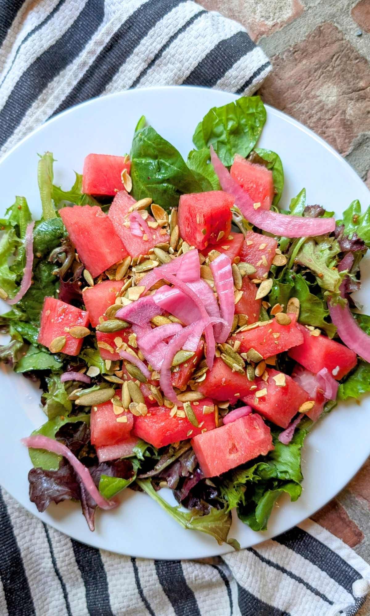 low sodium salad with fresh watermelon and spring mix greens with nuts on top.