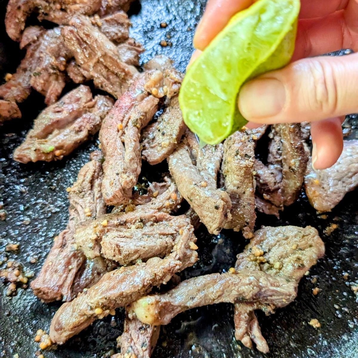 a hand squeezing fresh lime juice over seared flank steak for low sodium lunch bowls.