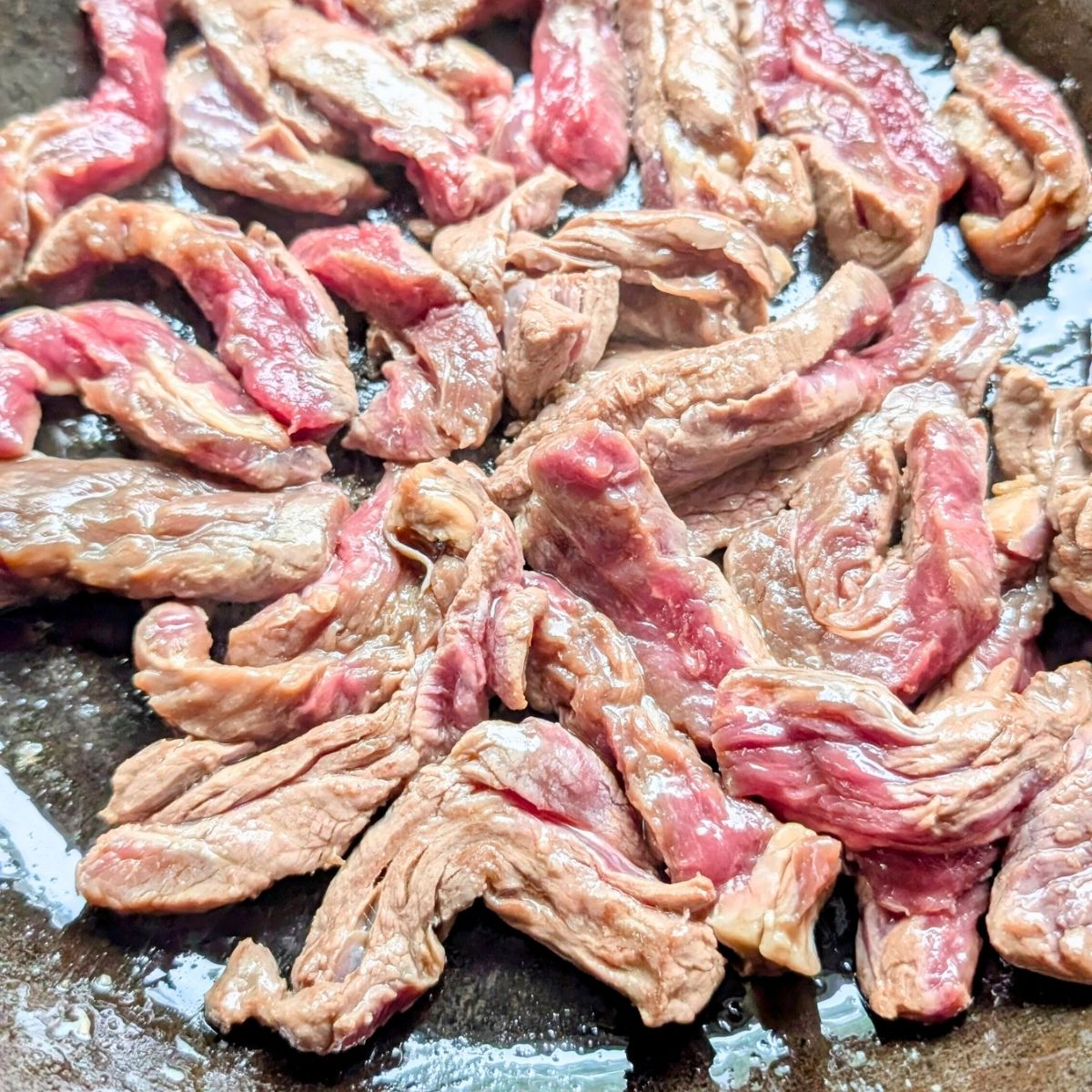 slices of flank steak in a cast iron skillet browning and searing.