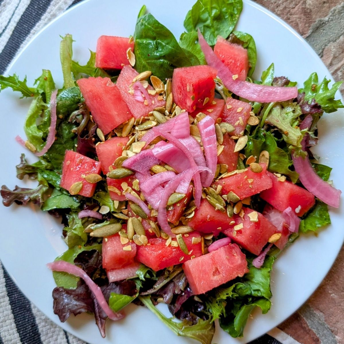 low sodium salad with watermelon, mixed greens, and pumpkin seeds on a plate.